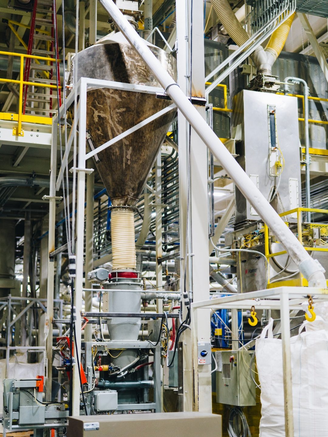 Tall interior processing tower with a worker at its base beside a bulk bag filling station
